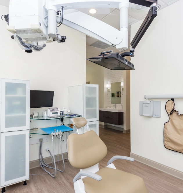 Modern dental operatory with overhead surgical light, beige chair, and sterilization equipment in clinical setting.