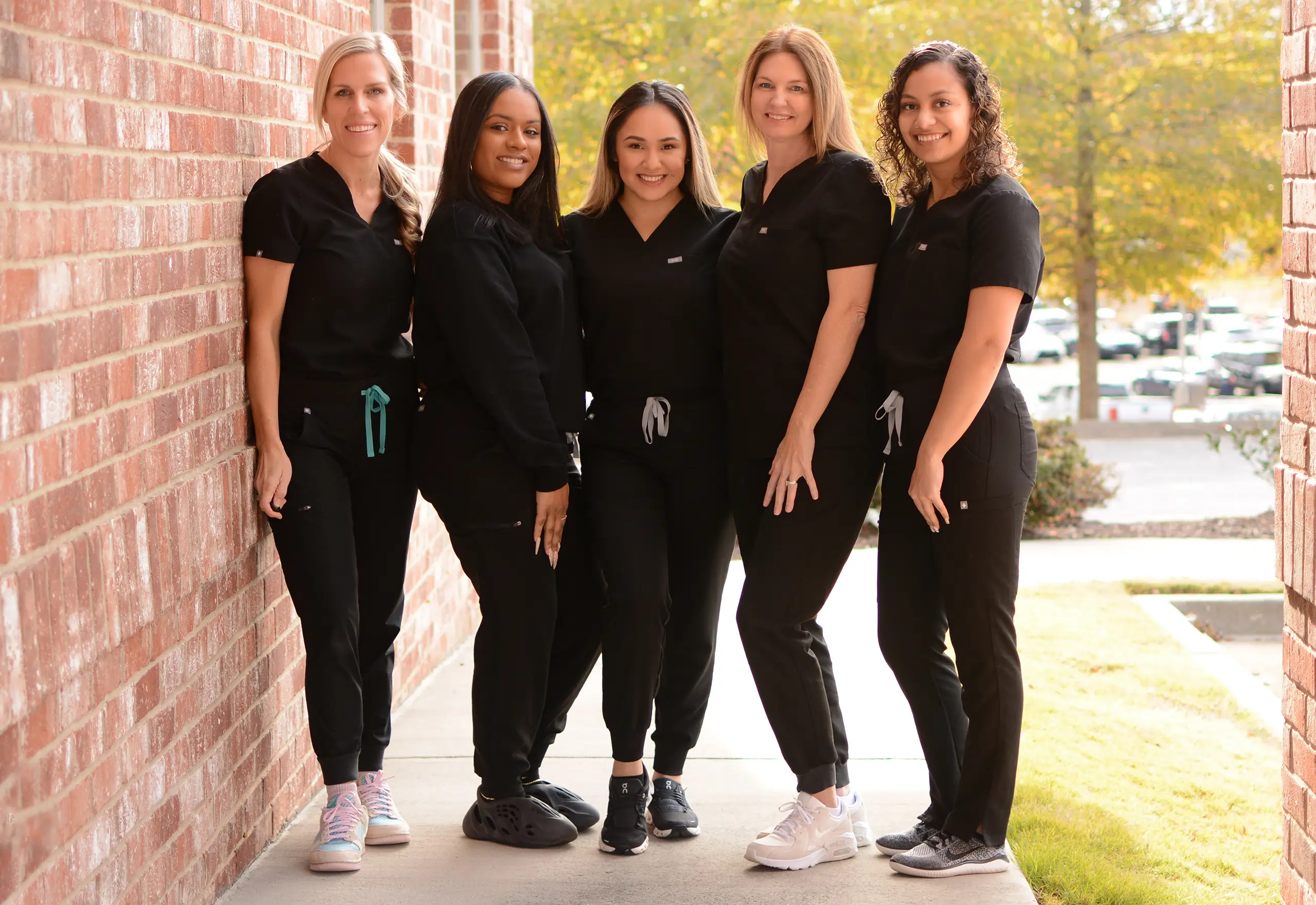 Five dental professionals in black uniforms stand together outside a brick building.